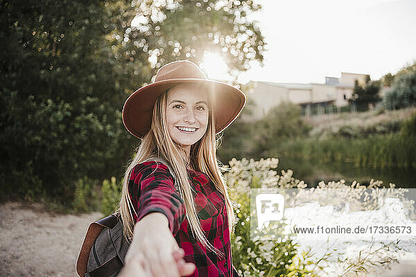 Glückliche schöne Frau mit Hut,  die bei Sonnenuntergang die Hand eines Freundes hält