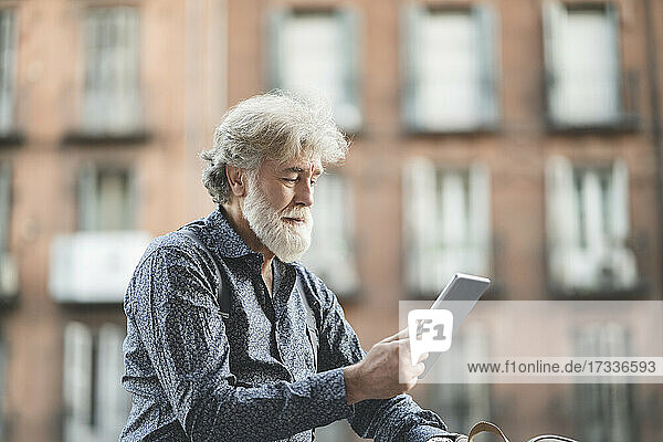 Älterer Mann mit weißen Haaren  der in der Stadt ein digitales Tablet benutzt