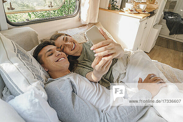 Happy woman taking selfie with boyfriend while lying on bed in motor home