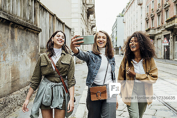 Happy woman taking selfie with friends through smart phone in city