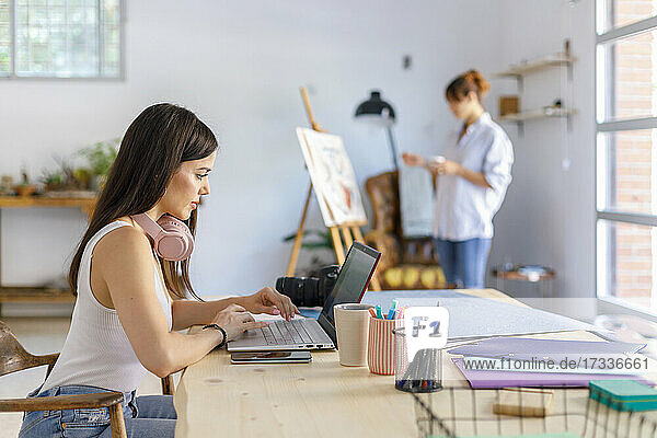 Fotografin benutzt Laptop  während Künstlerin im Atelier malt