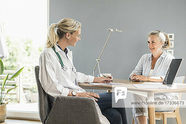 Weiblicher Arzt im Gespräch mit einem Patienten  während er im Büro sitzt
