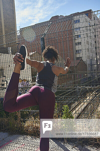 Female athlete doing stretching exercise while leaning on fence