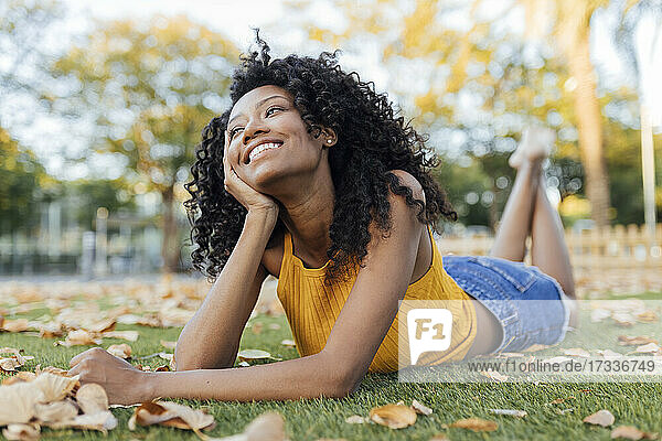 Thoughtful smiling young woman looking away while lying on grass at park