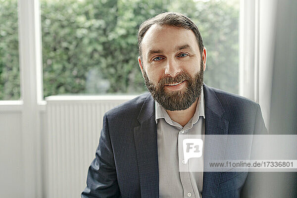 Smiling bearded mature businessman sitting in office