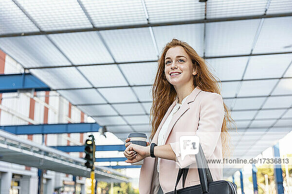 Lächelnde weibliche Fachkraft  die beim Warten auf dem Bahnsteig wegschaut