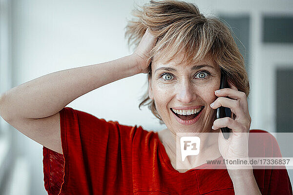 Geschäftsfrau mit Hand im Haar  die im Büro mit einem Mobiltelefon spricht