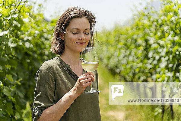 Smiling woman smelling wine while standing at vineyard
