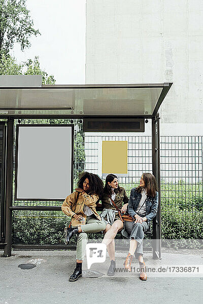 Women talking while sitting at bus stop