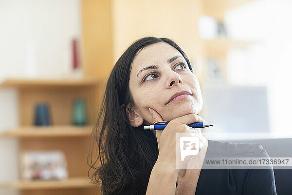Thoughtful female professional with hand on chin looking away while sitting in office