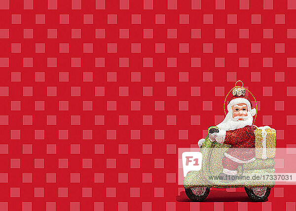 Weihnachtsschmuck von Santa Claus fahren Motorroller gegen lebendige rote karierten Hintergrund