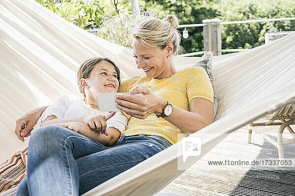 Lächelnde Tochter schaut ihre Mutter an  während sie sich in der Hängematte auf dem Balkon ausruht