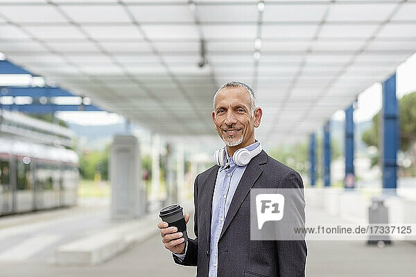 Lächelnder Geschäftsmann mit wiederverwendbarem Becher am Bahnhof