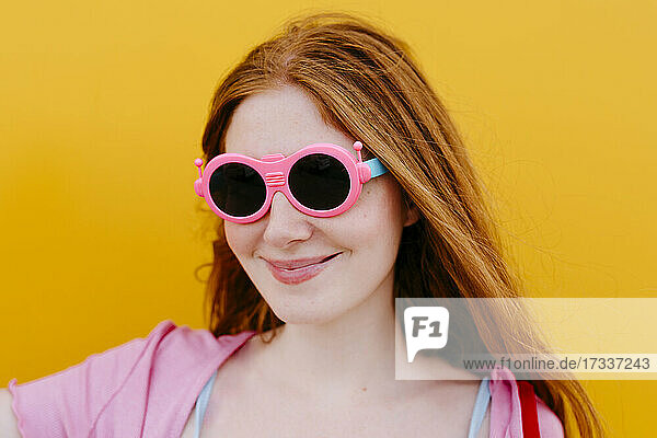 Frau mit rosa Sonnenbrille lächelnd vor gelber Wand