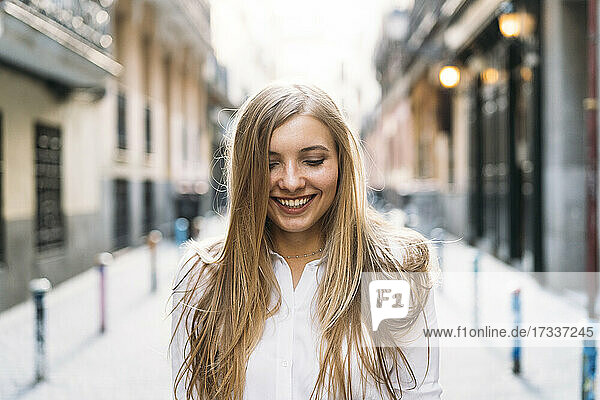 Cheerful young woman with blond hair standing at alley