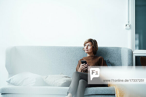 Thoughtful businesswoman with mobile phone sitting on sofa