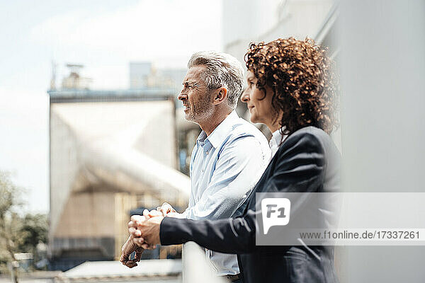 Thoughtful businessman standing with colleague by railing