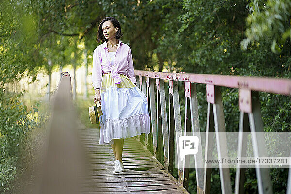 Junge Frau schaut weg  während sie auf einer Fußgängerbrücke in der Natur spazieren geht