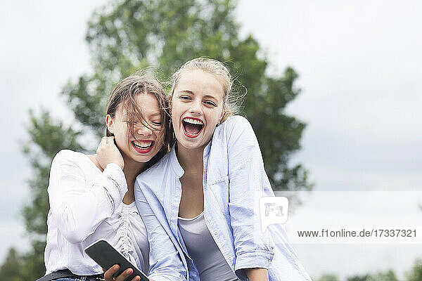 Female friends laughing while holding smart phone in nature