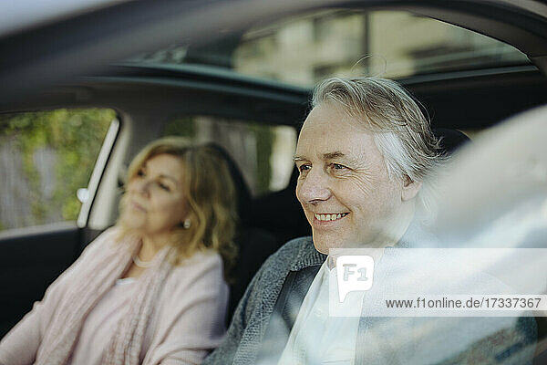 Smiling mature man sitting with woman in car seen through glass window