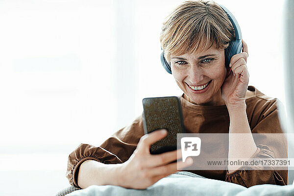 Smiling businesswoman using mobile phone while listening through headphones in office
