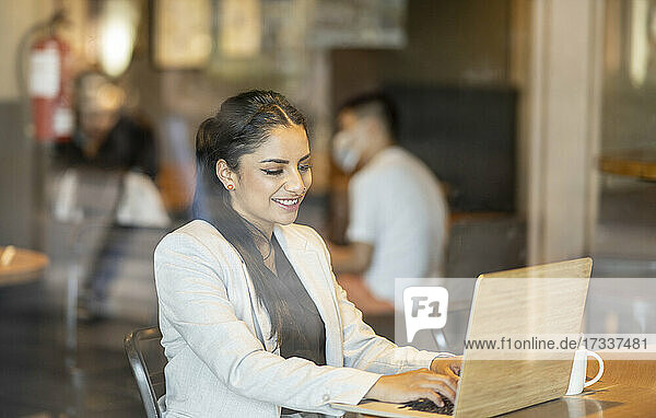 Weibliche Fachkraft  die einen Laptop benutzt  während sie in einem Café sitzt  gesehen durch ein Fensterglas