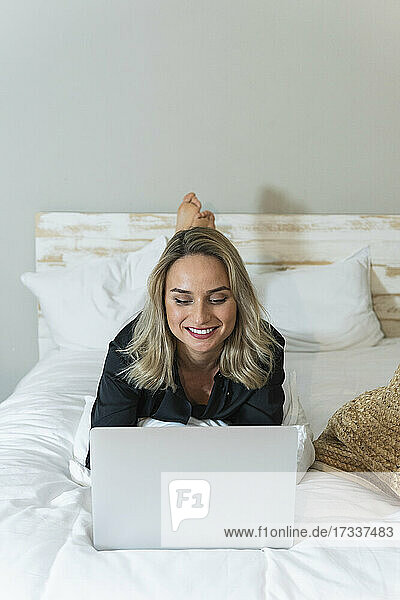 Geschäftsfrau arbeitet am Laptop  während sie zu Hause auf dem Bett liegt