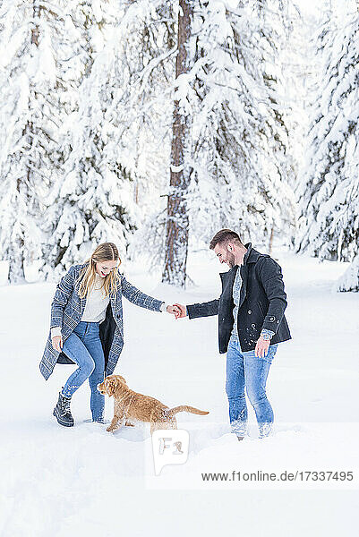 Ehepaar spielt mit Hund im Schnee während des Urlaubs