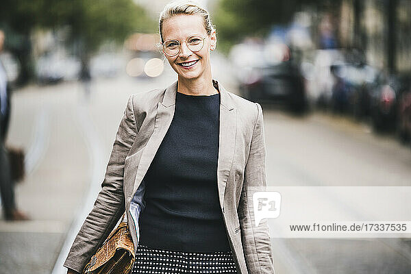 Lächelnde reife Geschäftsfrau  die eine Tasche hält  während sie auf der Straße steht