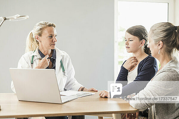Arzt mit Laptop betrachtet Patient und Frau im Büro