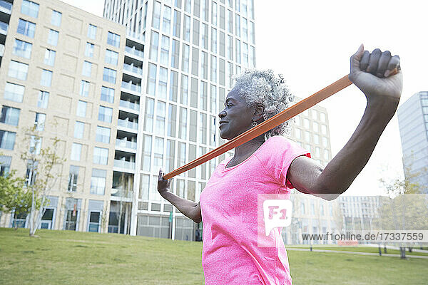 Aktive ältere Frau  die ein Widerstandsband zieht  während sie im Park trainiert