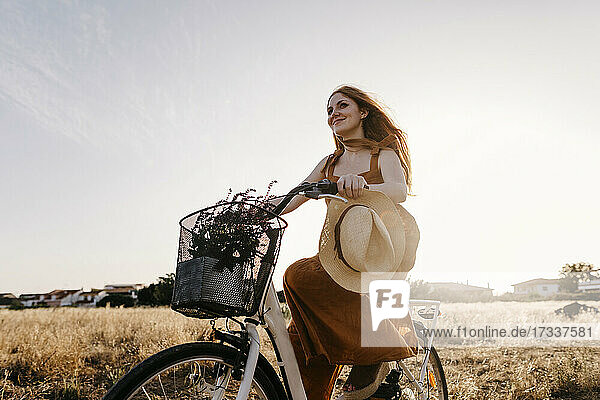 Rothaarige Frau fährt bei Sonnenuntergang Fahrrad in einem Feld