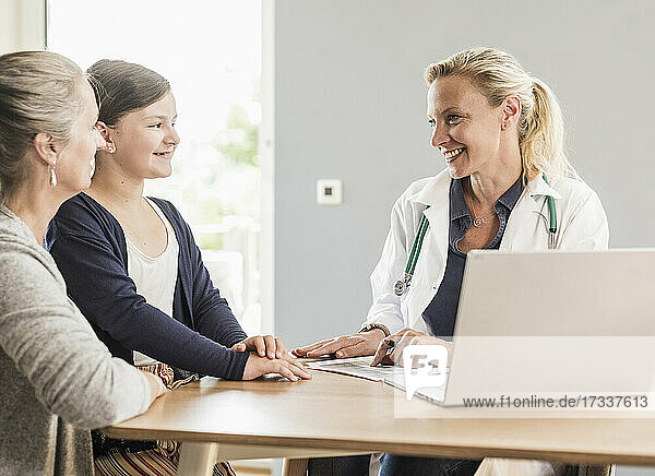 Lächelnde Ärztin betrachtet ein Mädchen  das mit seiner Mutter im Büro sitzt