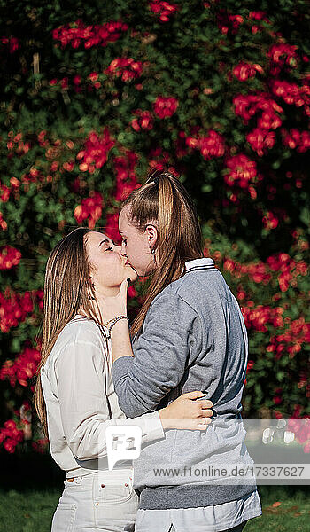 Frauen  die sich küssen  während sie vor einer blühenden Pflanze im Park stehen