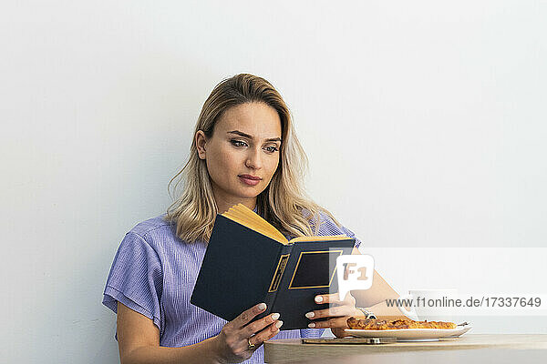 Beautiful woman reading book in front of wall at coffee shop