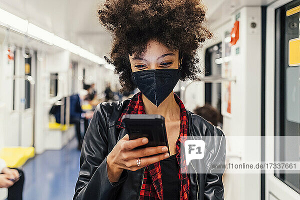 Frau mit Gesichtsmaske benutzt Mobiltelefon in der U-Bahn