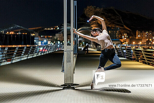 Frau mit geschlossenem Auge tanzt nachts auf der Seebrücke