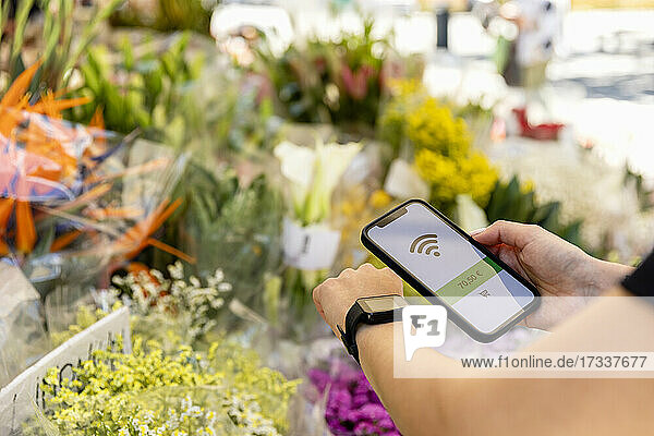 Frau beim kontaktlosen Bezahlen mit Smartwatch und Mobiltelefon im Blumenladen