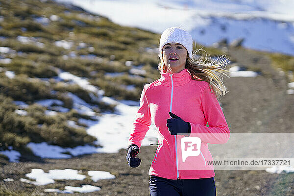 Junge Sportlerin läuft im Winter an einem sonnigen Tag auf einem Berg