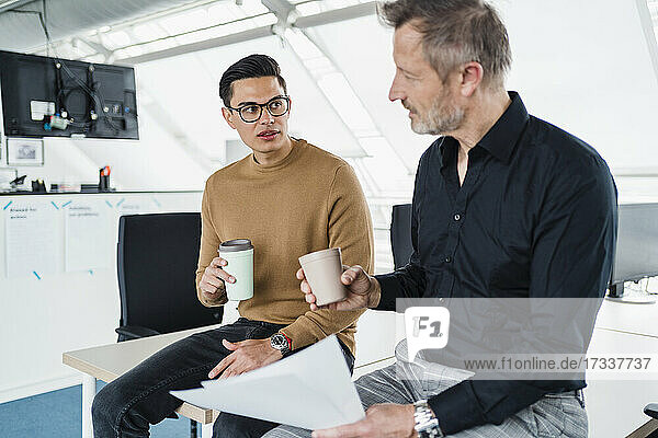 Businessmen with coffee cup having discussion while sitting on desk
