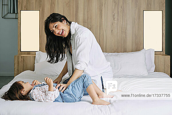 Cheerful mother and daughter playing over bed at home
