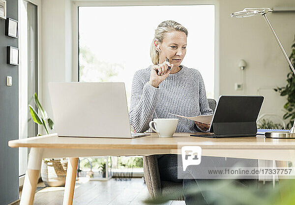 Geschäftsfrau mit digitalem Tablet und Laptop  die Papier bei der Arbeit im Büro zu Hause hält