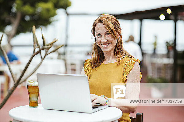 Female freelance worker sitting with laptop and drink at bar