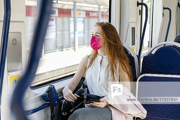 Geschäftsfrau mit Gesichtsschutzmaske schaut beim Pendeln im Zug durch das Fenster