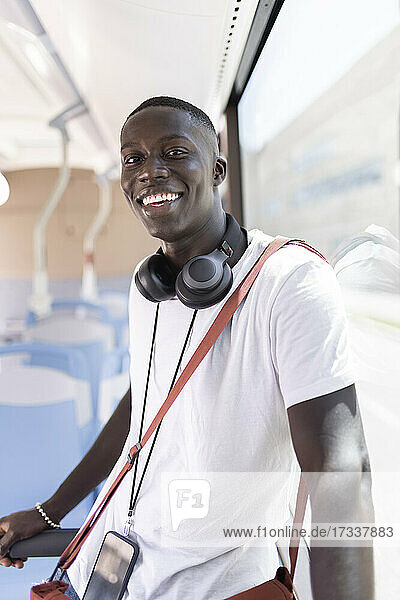 Lächelnder männlicher Profi mit Umhängetasche und Kopfhörern im Bus