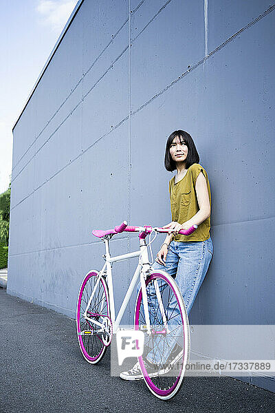 Junge Frau schaut weg  während sie sich mit dem Fahrrad an die Wand lehnt