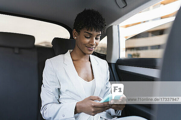 Geschäftsfrau  die im Auto sitzend ihr Smartphone benutzt