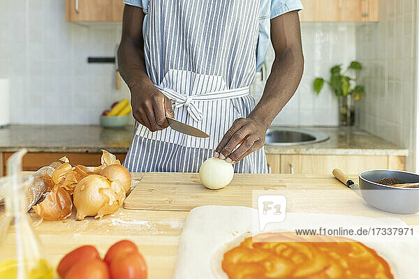 Mann schneidet Zwiebel bei der Zubereitung von Pizza in der Küche zu Hause