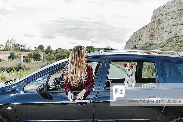 Glückliche junge blonde Frau und Hund am Autofenster