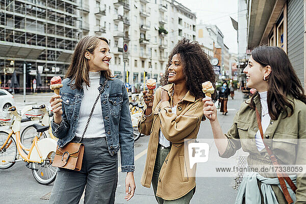 Lächelnde Freunde essen Eis beim Spaziergang in der Stadt Straße